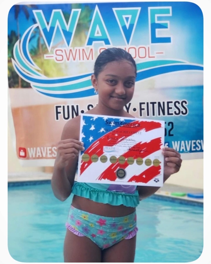 A WAVE swimmer proudly holding her certificate in front of the WAVE banner